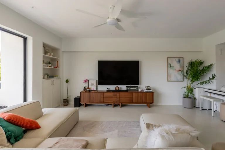 Bright living room with a cream sectional sofa, a long wood-toned TV console on pale large-format floor tiles and a white ceiling fan